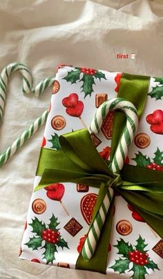 a present wrapped in wrapping paper with candy canes and holly decorations on it, sitting on a bed