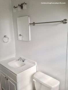 a white toilet sitting next to a sink in a bathroom under a mirror and towel bar