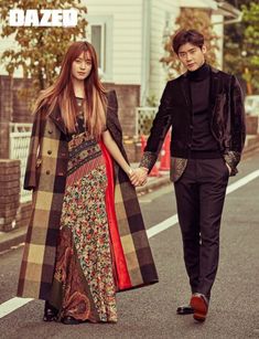 two people are walking down the street holding hands and one is wearing a long coat