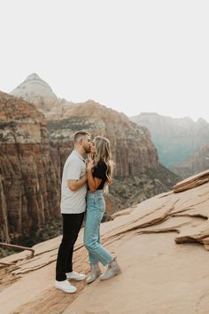 a man and woman standing on top of a mountain kissing in front of the mountains