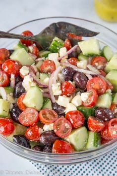 a salad with cucumbers, tomatoes, onions and olives in a glass bowl