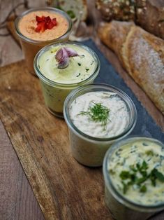 three different types of dips on a wooden board with bread in the back ground