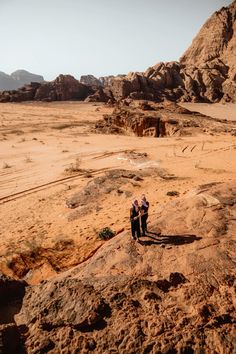 two people standing on top of a large rock in the middle of a desert area