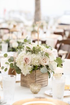 a centerpiece with white flowers and greenery sits on a table at a wedding reception