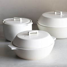 three white casseroles sitting on top of a table next to each other with lids