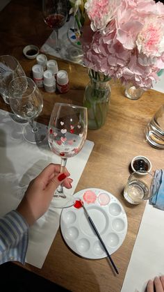 a person is holding a wine glass on a table with flowers in vases behind them