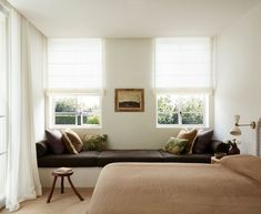 a bed sitting under two windows next to a window sill with pillows on it