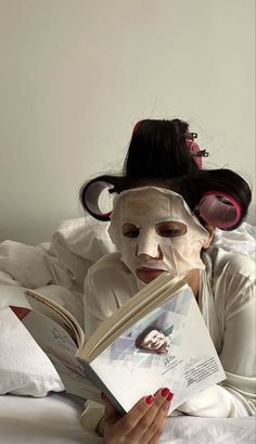 a woman laying in bed reading a book with her face painted like a monkey on top of it