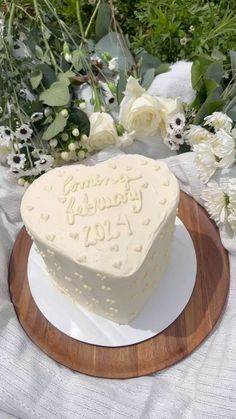 a heart shaped cake sitting on top of a wooden platter next to white flowers