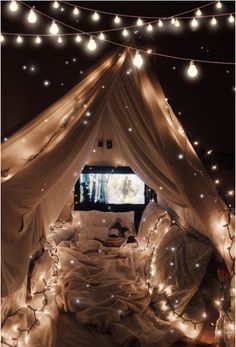 a bed covered in white sheets and lights under a canopy with a tv on it