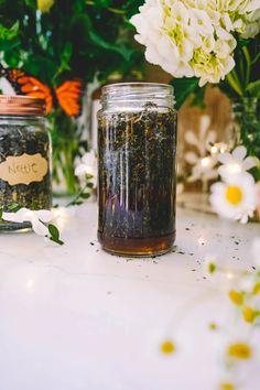 two jars filled with tea sitting on top of a table next to flowers and butterflies