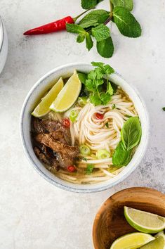 a bowl of soup with meat, noodles and garnishes on the side