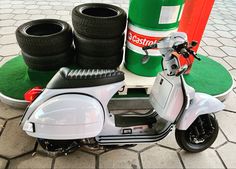 a white scooter parked next to some tires on the ground near a green barrel