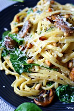 pasta with mushrooms, spinach and parmesan cheese on a blue plate sitting on a white tablecloth