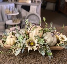 an arrangement of flowers and pumpkins on a table in a room with other furniture