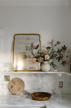 a vase with flowers and a wooden bowl on a marble counter top in a kitchen