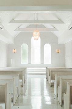 an empty church with white pews and chandelier