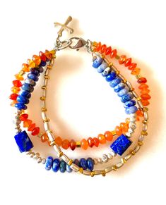 Trio of beaded bracelets featuring lapis lazuli, denim blue sodalite and carnelian and Karen Hill Tribe fine silver and gold vermeil. One strand is natural orange carnelian translucent faceted 6mm rondelles accented with Karen Hill Tribe 24k gold vermeil cubes. A second strand is shades of denim and cobalt blue 6.5mm smooth sodalite rondelles and deep blue lapis lazuli free form tube beads accented smith Karen Hill Tribe .999 fine silver faceted cubes and flower beads. Third strand is silver and Spiritual Sapphire Beaded Bracelets With Natural Stones, Bohemian Lapis Lazuli Gemstone Bracelets, Handmade Bohemian Lapis Lazuli Bracelets, Bohemian Blue Beaded Bracelets With Gemstone, Artisan Blue Gemstone Beaded Bracelets, Blue Bohemian Bracelets With Polished Beads, Sapphire Lapis Lazuli Beaded Bracelets, Sapphire Lapis Lazuli Gemstone Beaded Bracelets, Blue Carnelian Spiritual Jewelry