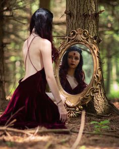 a woman sitting in the woods looking at herself in a mirror