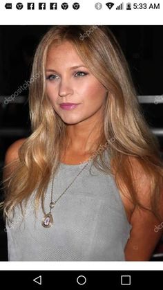 a woman with long blonde hair wearing a gray top and necklace smiling at the camera