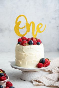 a cake topped with berries and blueberries on top of a white plate next to a cupcake