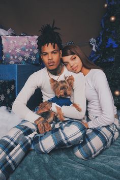 a man and woman sitting on a bed with their dog in front of christmas presents