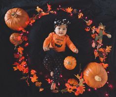 a baby sitting in a pumpkin wreath surrounded by fall leaves and pumpkins on a black background