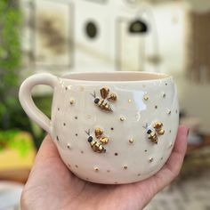 a hand holding a coffee cup with bees on it and gold flecks around the rim