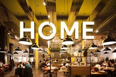 the inside of a restaurant with people sitting at tables and hanging lights above it that read home