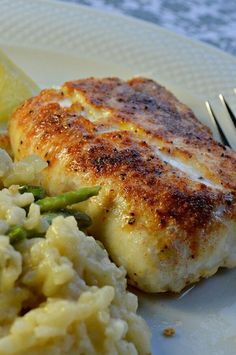 a white plate topped with chicken, rice and asparagus next to lemon wedges