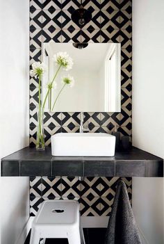 a white sink sitting under a mirror next to a black and white tiled wallpaper