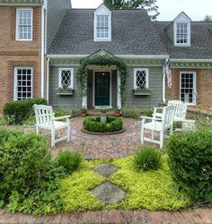 two white chairs sitting on top of a brick walkway in front of a gray house