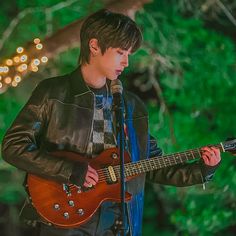 a young man holding a guitar while standing in front of a microphone