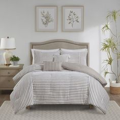 a bed with white and grey striped comforter in a bedroom next to two plants