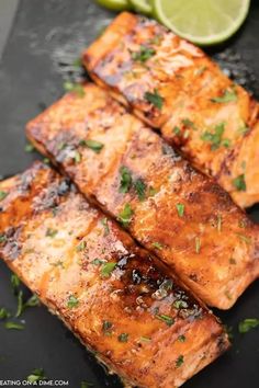 grilled salmon on a black plate with limes and cilantro