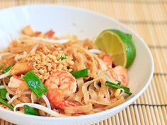 a white bowl filled with noodles and shrimp next to a lime wedge on top of a table