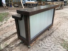 a bar made out of corrugated metal and wooden planks on the beach with people in the background