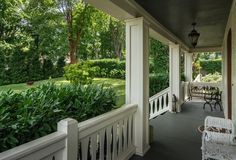 the porch is covered with white railings and has chairs on each side, along with greenery