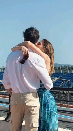 a man and woman embracing each other on the roof of a building in front of a stadium