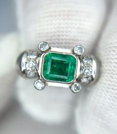 an emerald and diamond ring on top of a white cloth with diamonds around it's edges