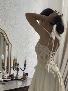 a woman standing in front of a mirror wearing a white dress and holding her hands to her head