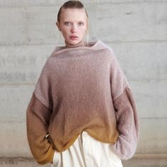 a woman standing in front of a wall wearing a brown and tan sweater with an asymmetrical design