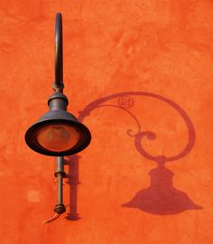 the shadow of a lamp post on an orange wall is cast by a street light