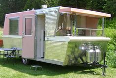 a pink and silver trailer parked on top of a lush green field