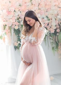 a pregnant woman wearing a pink gown and holding her belly in front of a floral backdrop