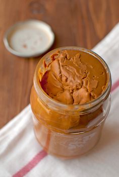 a jar filled with peanut butter sitting on top of a wooden table next to a spoon