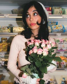 a woman holding a bouquet of pink roses in front of a store display case with other items