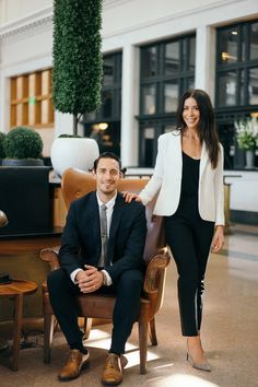 a man and woman are posing for a photo in an office setting with chairs, tables, and potted plants