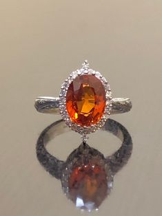 DeKara Designs Collection Our latest design! An elegant and lustrous Opal cabochon and diamond hand engraved platinum engagement ring. Metal- 90% Platinum, 10% Iridium. Stones- Genuine Oval Orange Sapphire 2.50 Carats. 24 Round Diamonds F-G Color VS1-VS2 Clarity 0.25 Carats. Latest of my creations! A Beautiful Handmade Hand Engraved Orange Sapphire Halo Diamond Engagement Ring Made in Platinum. The fiery Orange Sapphire is oval in shape and professionally prong set in between two unique triple p Luxury White Gold Topaz Ring With Halo Setting, Wedding Ruby Ring With Platinum Accent Stones, Luxury 14k White Gold Topaz Wedding Ring, Formal Orange Diamond Ring, Formal Orange Rings With Halo Setting, Luxury White Gold Halo Ring With Accent Stones, Luxury Orange Rings With Prong Setting, Luxury Topaz Ring With Halo Design, Luxury Topaz Ring With Halo Design For Formal Occasions