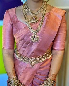 a woman in a pink sari with gold jewelry on her neck and hands behind her back